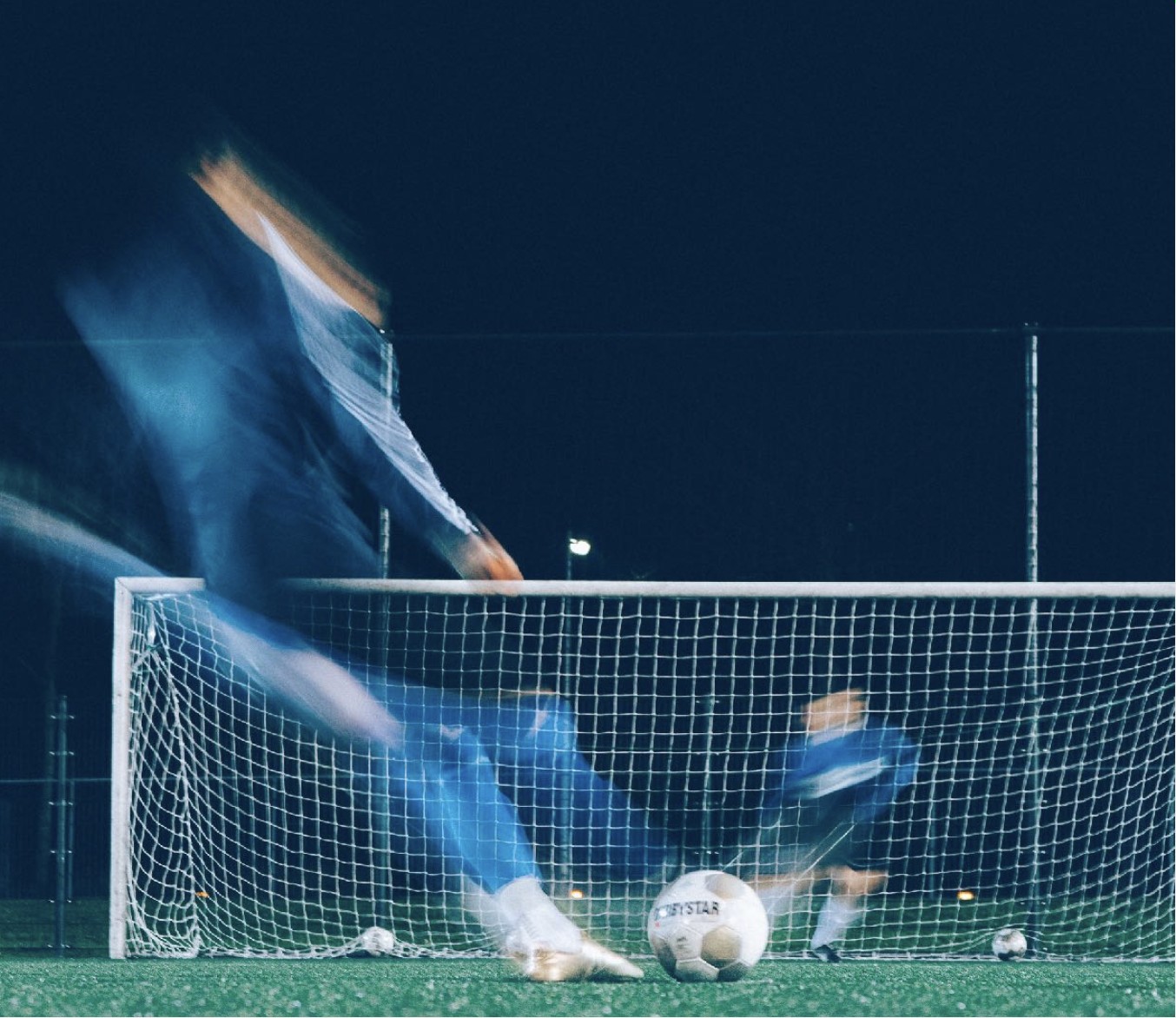 A football goal on an artificial pitch under floodlights at night – a player moving towards the ball