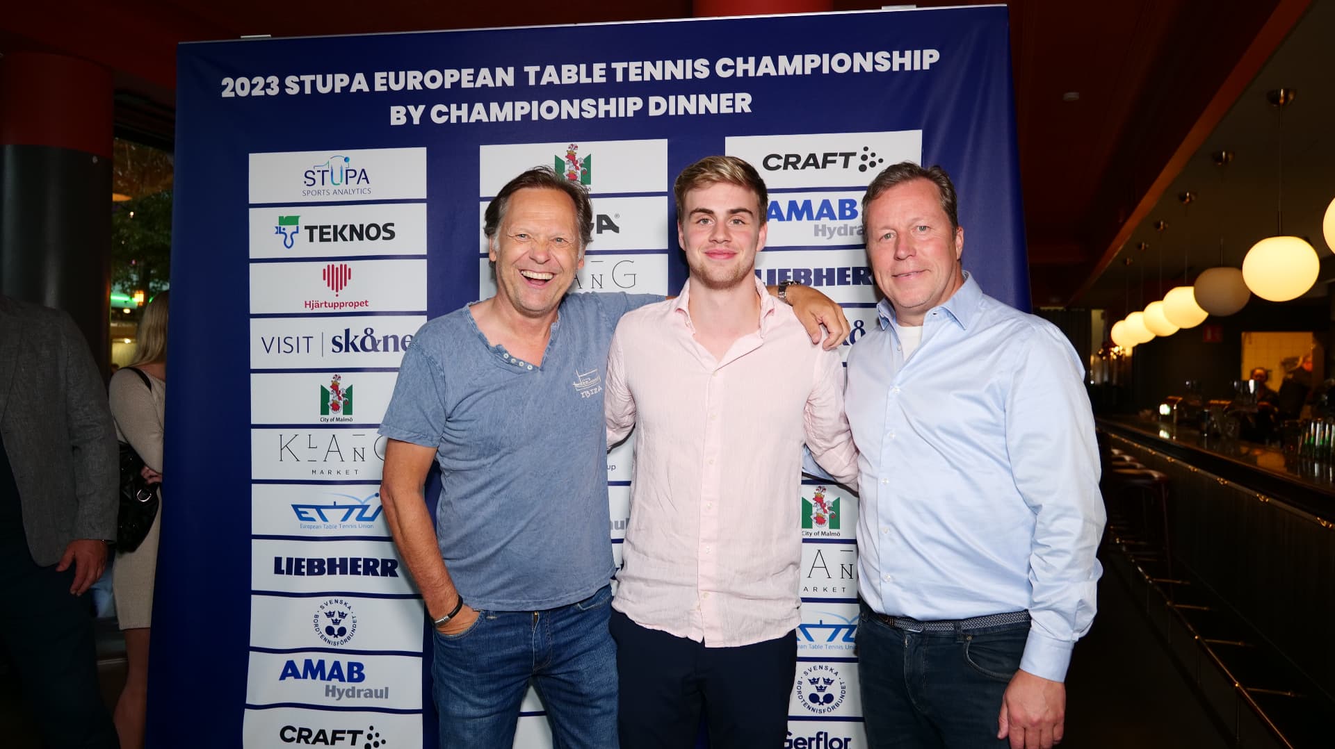 Guests in front of the sponsor wall for the 2023 STUPA European Table Tennis Championship at the World Champions' Dinner